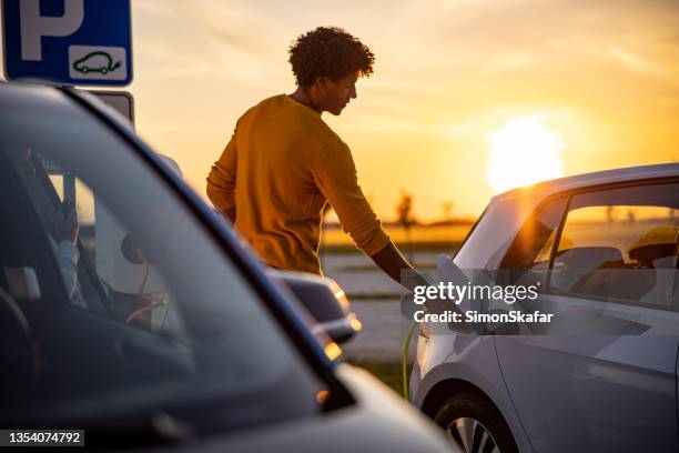 african american man inserting plug into the electric car charging socket - elektrische auto stockfoto's en -beelden