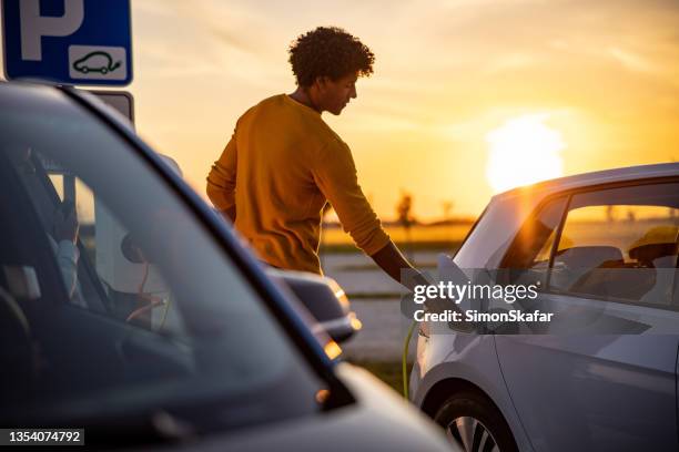 african american man inserting plug into the electric car charging socket - electric vehicle bildbanksfoton och bilder