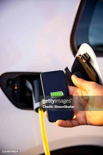 charging an electric car with mobile phone screen showing full battery - electric car black stock pictures, royalty-free photos & images