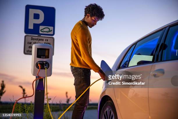 african american man inserting plug into the electric car charging socket - tesla motors stock pictures, royalty-free photos & images