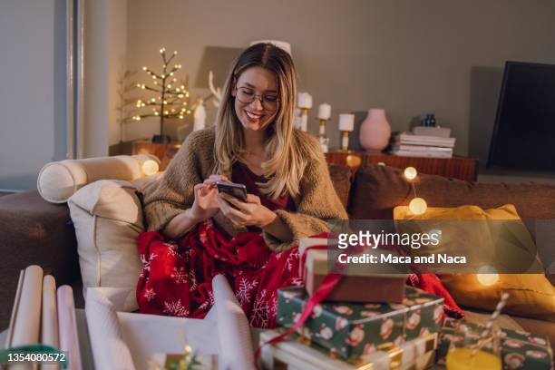 young woman uses mobile phone at home during winter holidays - chat noel stockfoto's en -beelden