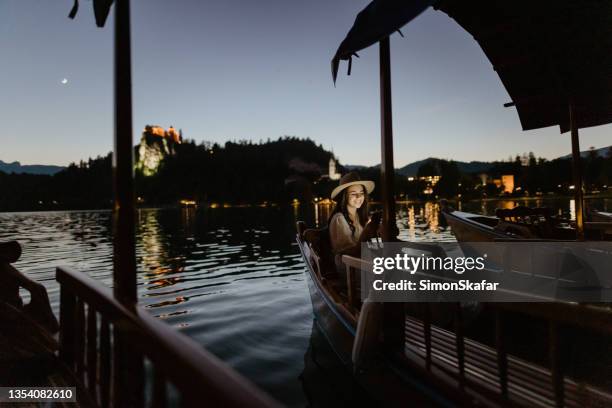 junge frau mit handy auf holzboot - bled slovenia stock-fotos und bilder