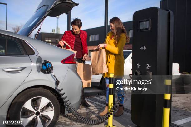 photo of a young couple on a parking lot, charging their electric car - red car wire stock pictures, royalty-free photos & images