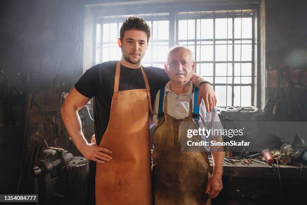 portrait of grandfather and grandson blacksmith with arm around shoulders - successor stock pictures, royalty-free photos & images