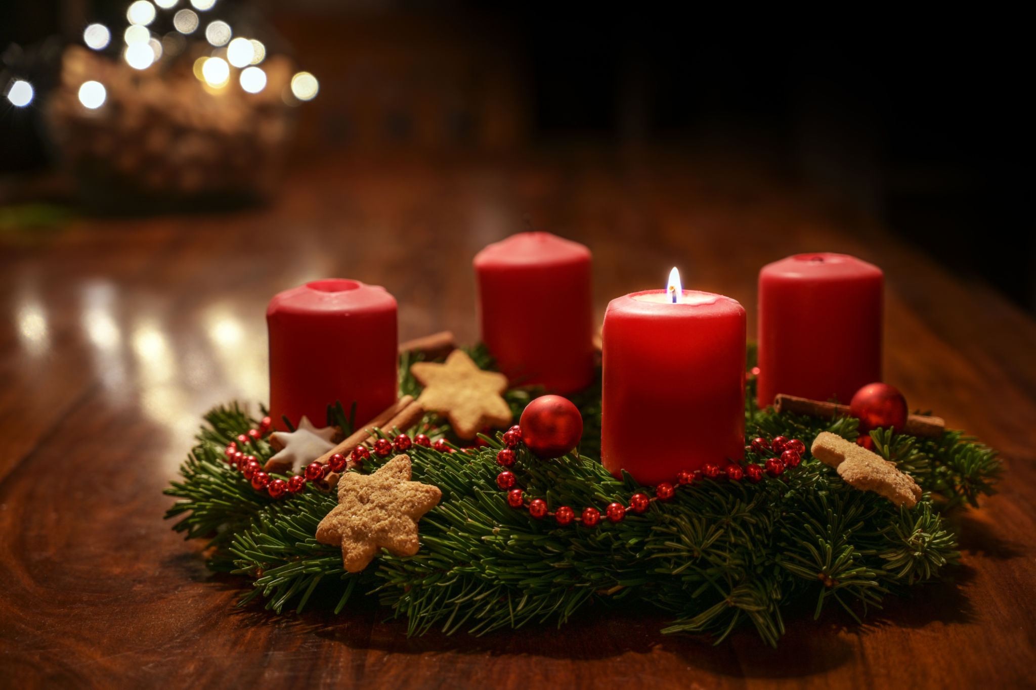 First Advent - decorated Advent wreath from fir branches with red burning candles on a wooden table in the time before Christmas, festive bokeh in the warm dark background, copy space, selected focus First Advent - decorated Advent wreath from fir branches with red burning candles on a wooden table in the time before Christmas, festive bokeh in the warm dark background, copy space, selected focus