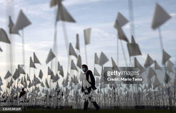 Person wearing a face covering walks past a white flag memorial installation outside Griffith Observatory honoring the nearly 27,000 Los Angeles...