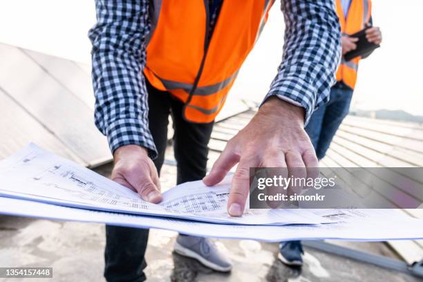 male engineer holding plan while standing on the rooftop of solar power plant. - lower stockfoto's en -beelden