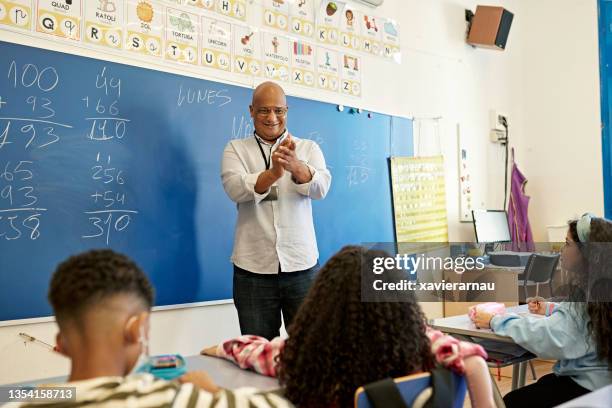 maestra sonriente aplaudiendo a joven estudiante en el aula - many teachers networking fotografías e imágenes de stock