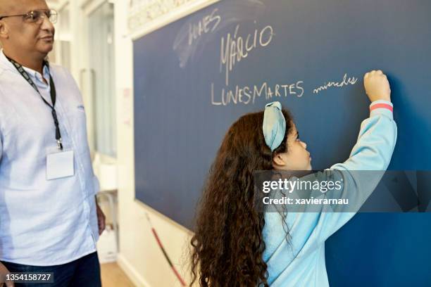 teacher watching 7 year old girl write on board - spanish language stock pictures, royalty-free photos & images