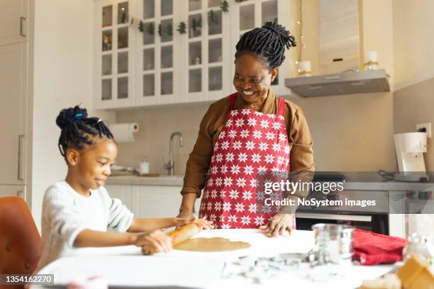 little girl making christmas gingerbread cookies with a grandmother - black grandma stockfoto's en -beelden