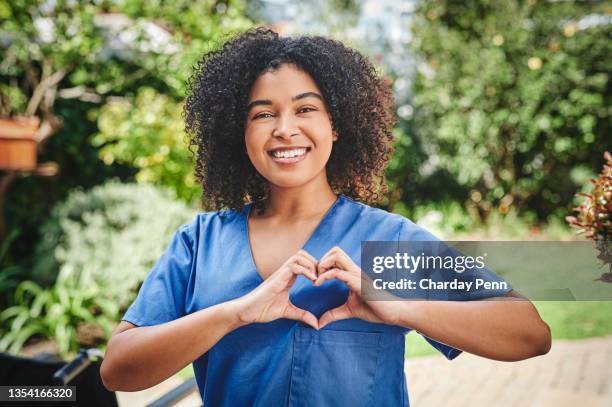 shot of an attractive young nurse standing alone outside and making a heart shaped gesture - hart stockfoto's en -beelden