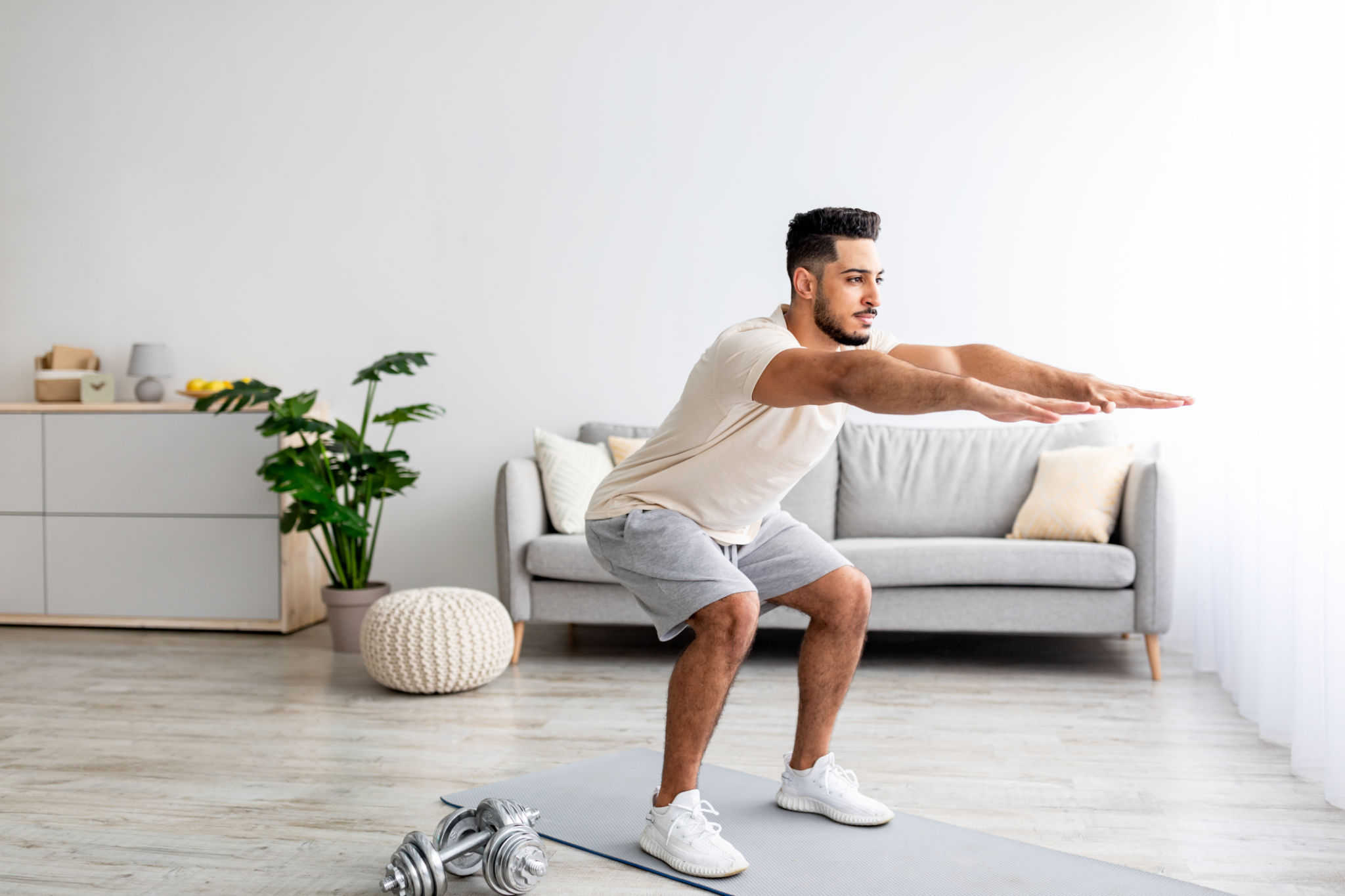 Handsome young Arab man doing squats at home Handsome young Arab man doing squats at home