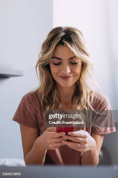 a blonde woman texting and smiling - scrollen stockfoto's en -beelden