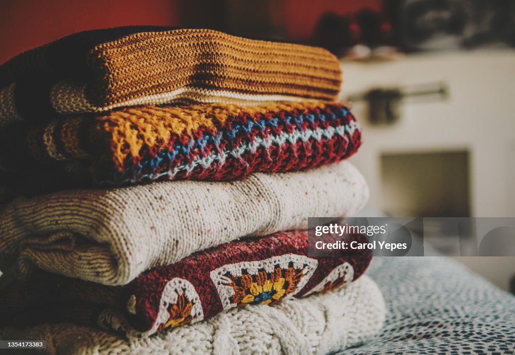 Cozy fall sweaters folded and stacked up on table by window at bedroom