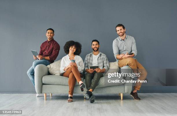 portrait en pied d’un groupe jeune et diversifié d’hommes d’affaires utilisant leurs appareils sans fil assis sur un canapé sur un fond gris en studio - femme dans un groupe dhommes photos et images de collection