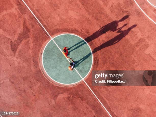 zwei freunde spielen zusammen basketball und halten sich vor dem start an den händen - luftbild - sports pitch stock-fotos und bilder