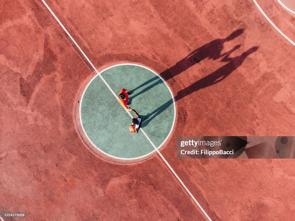 Two friends are playing basketball together, holding hands before the start - Aerial point of view