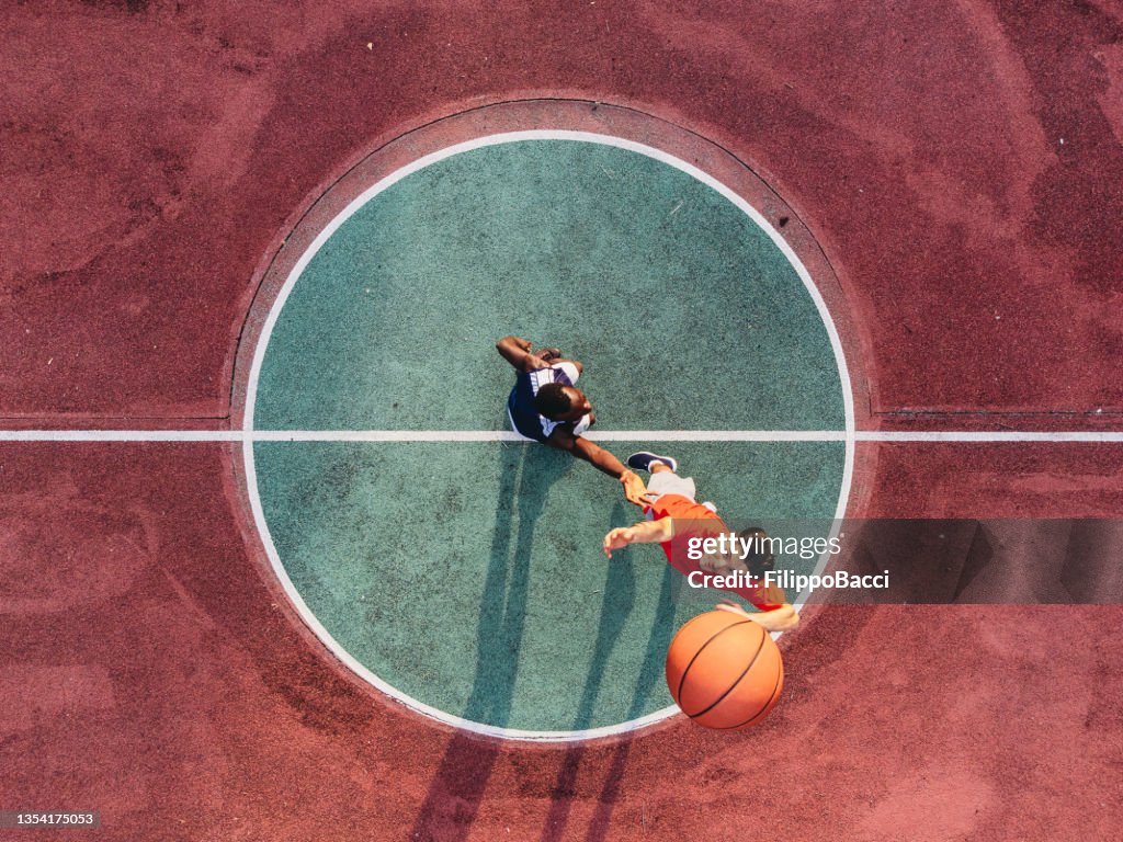 Two friends are jumping to take a basketball ball on the center field