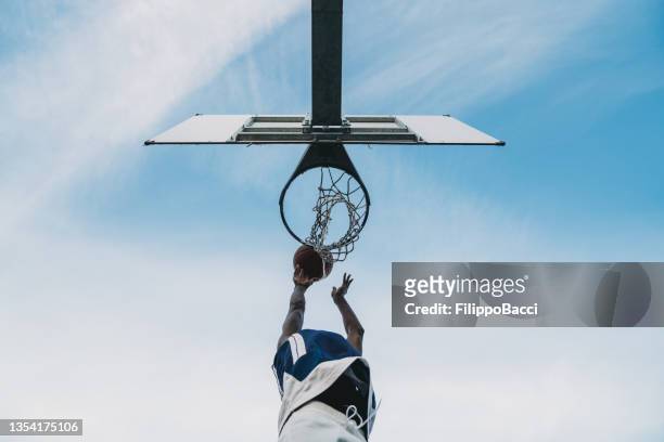 low angle view of a young adult man scoring a goal in a basketball court - back board stock pictures, royalty-free photos & images