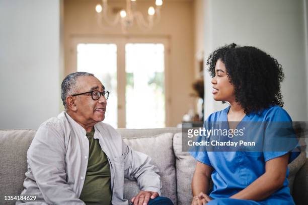 shot of an attractive young nurse sitting on the sofa with her senior patient and bonding with him - old man afro stock pictures, royalty-free photos & images