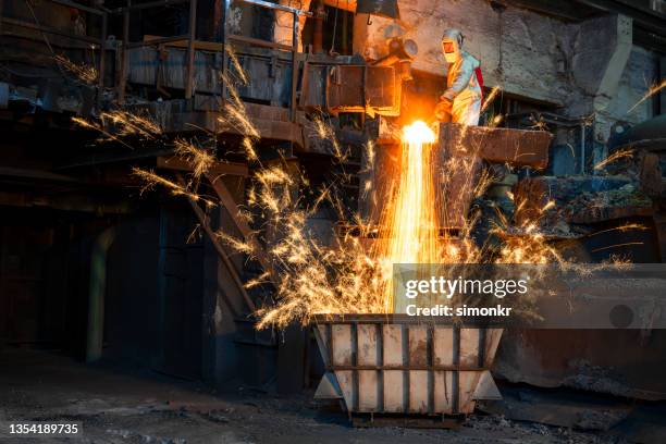 worker creating sparks pouring molten metal in container - steelmaking stock pictures, royalty-free photos & images