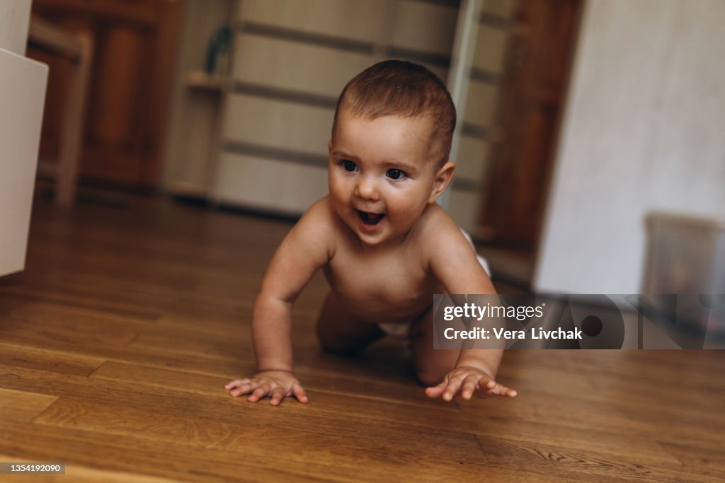 Little baby in diaper crawling on floor at home