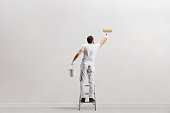 Rear view shot of a painter holding a bucket and painting a wall on a leader