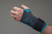 Velcro wrist stabilizer cast worn by Caucasian male hand. A blue split brace meant to aid Carpel Tunnel syndrome. Close up studio shot, isolated on gray background