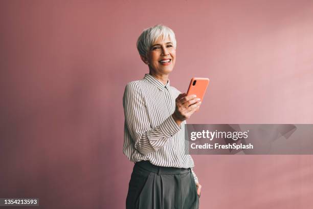 retrato de una mujer de negocios de alto nivel usando un teléfono móvil - mirando a la cámara fotografías e imágenes de stock
