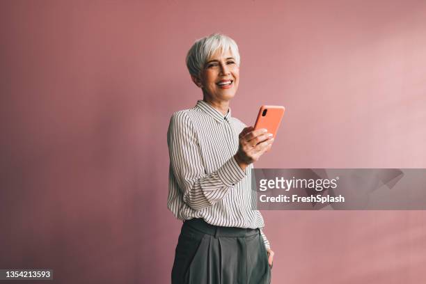 portrait d’une femme d’affaires senior utilisant un téléphone portable - fond studio photo photos et images de collection