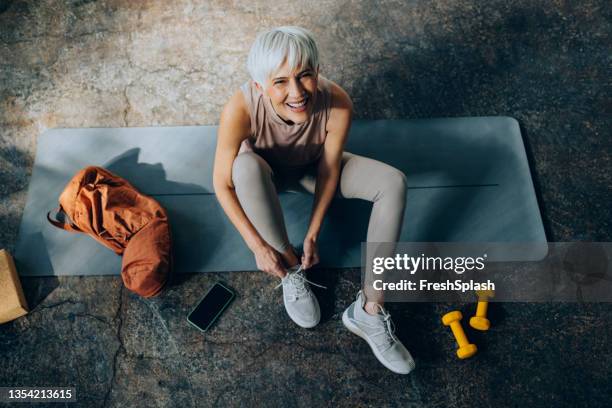 senior woman bindet vor dem home workout schnürsenkel an ihre turnschuhe - gray shoe stock-fotos und bilder