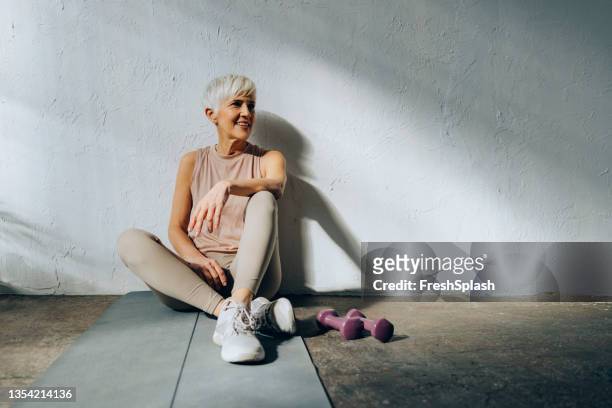 donna anziana sorridente seduta su un tappetino per esercizi - donne anziane foto e immagini stock