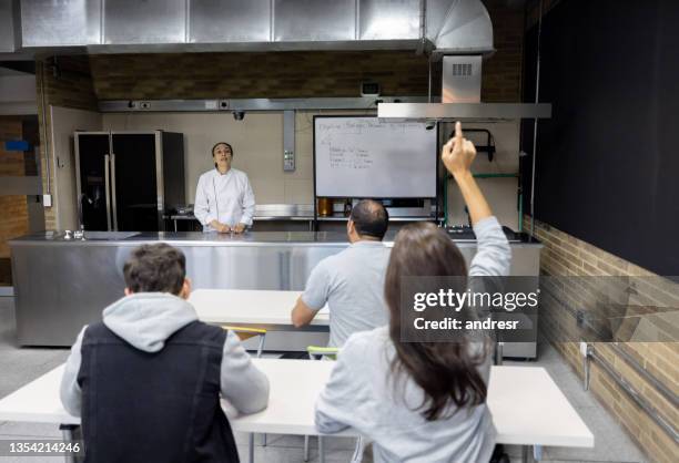 frau, die ihre hand hebt, um in einem kochkurs eine frage zu stellen - fragen beim kochen stock-fotos und bilder