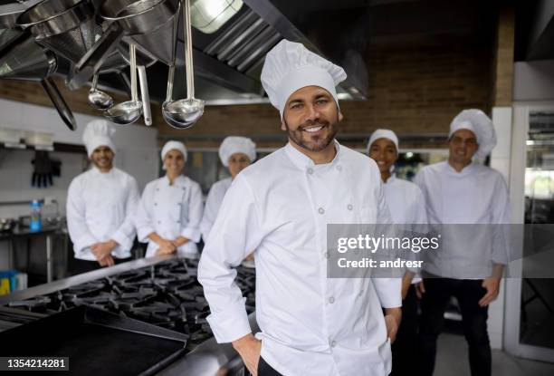 happy chef leading a group of cooks in the kitchen of a restaurant - chef male kitchen stock pictures, royalty-free photos & images