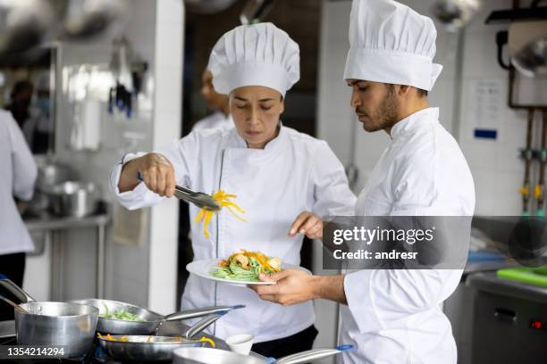köche servieren einen teller in der küche eines restaurants - young chefs cooking stock-fotos und bilder