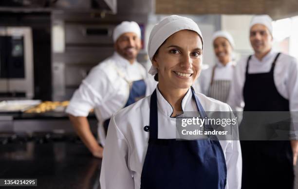 happy female baker working at a bakery with her team - apron stockfoto's en -beelden