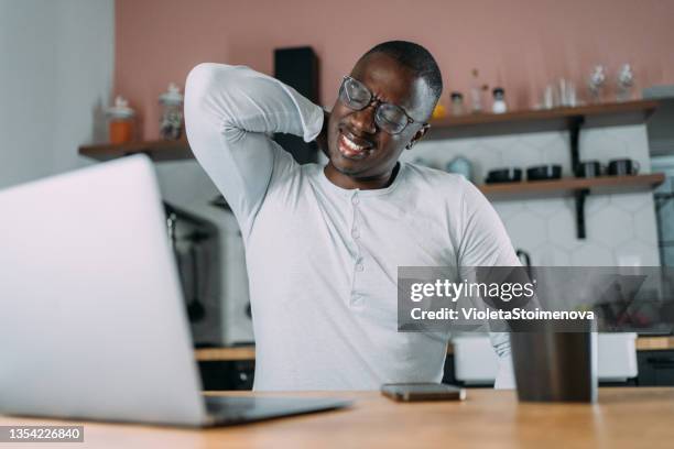 young man rubbing his neck while working from home. - má postura imagens e fotografias de stock