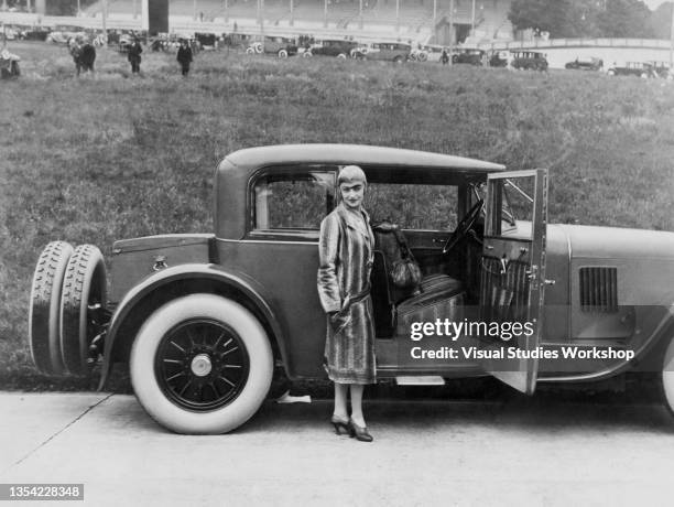 Portrait of French actress Nadine Picard , dressed in a python skin coat as she poses beside a Panhard et Levassor 20 CV Sport Special sedan at the...