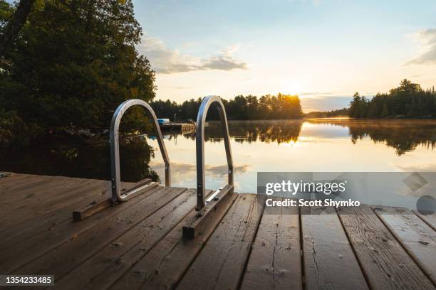 the sun rises over a dock on a calm lake - cottage dock stock pictures, royalty-free photos & images