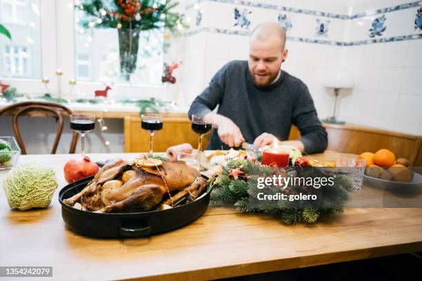 junger mann bereitet weihnachtsessen mit gänsebraten auf hölzernem küchentisch zu - gänsebraten stock-fotos und bilder