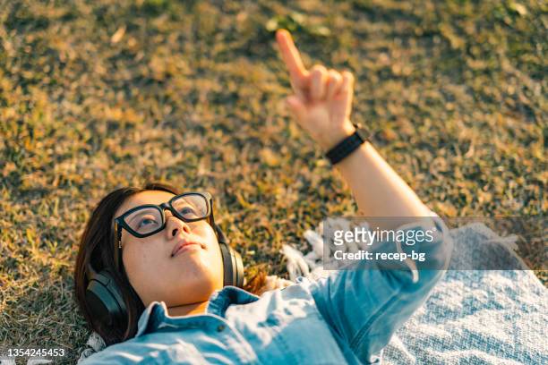young woman wearing smart glasses and laying down on grass and doing leisure activities on augmented reality metaverse - smart glasses stock pictures, royalty-free photos & images