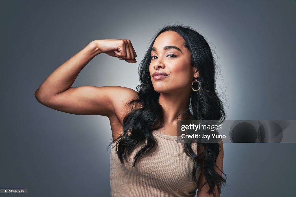 Studio shot of a beautiful young woman flexing while standing against a grey background