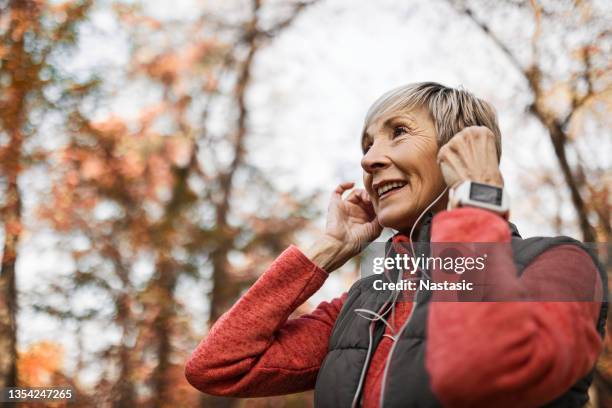 senior woman putting headphones on - senior women jogging stock pictures, royalty-free photos & images