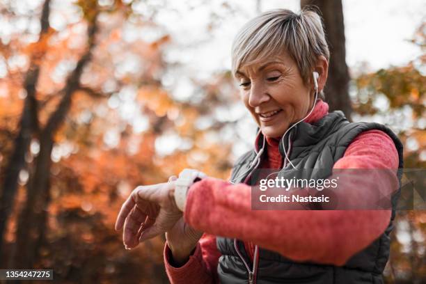 senior woman looking at smart watch wearing headphones - human neck stock pictures, royalty-free photos & images