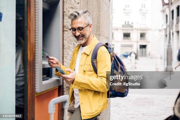 turista maduro tomando el dinero en el cajero automático - cajero fotografías e imágenes de stock