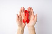 First person top view photo of young woman's hands holding red silk ribbon in palms symbol of aids awareness on isolated white background