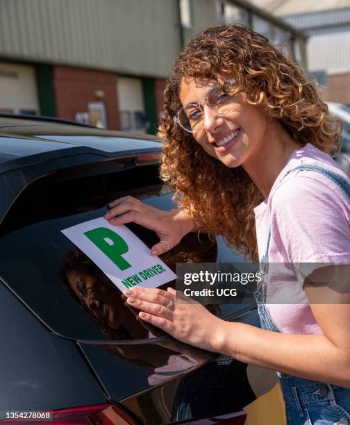 England, UK, New driver, young attractive woman holding a green new driver sign to display on her car after passing the driving test.