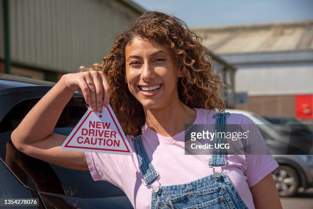 England, UK, New driver, young attractive woman holding a new driver caution sign to display on her car after passing the driving test.