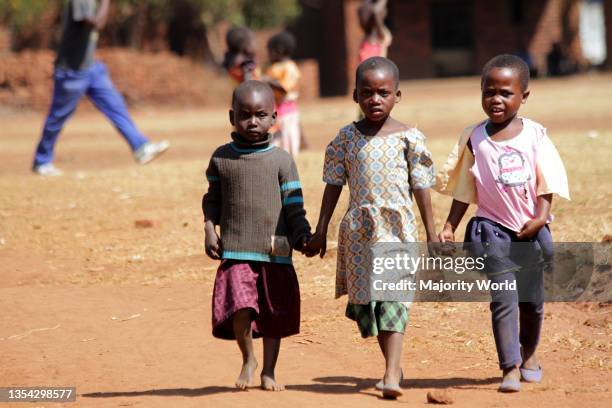 Three small girls are seen holding hands as they head home from a function at a community ground. Malingunde, Malawi.