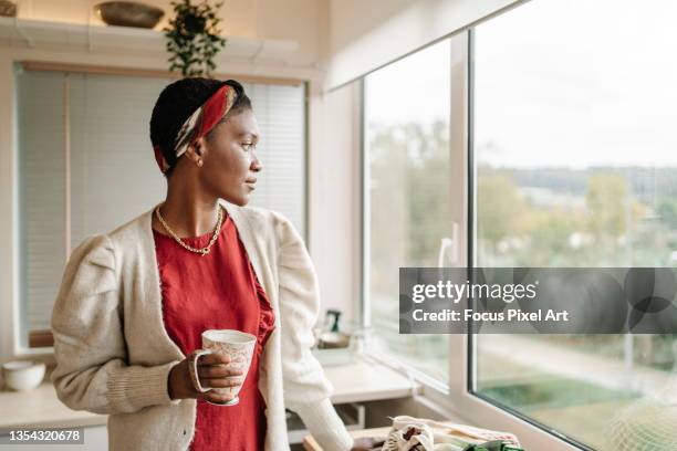black woman thinking and looking out the kitchen window. - guardare fuori dalla finestra foto e immagini stock